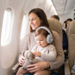 Toddler wearing grey ear defenders on a plane, calm on mum's lap