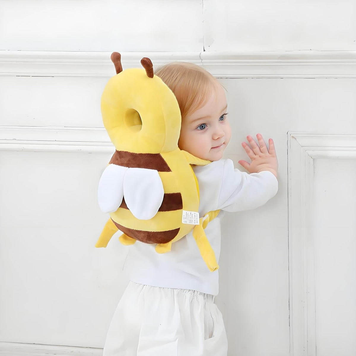 Toddler standing at a wall wearing the bee head protector backpack