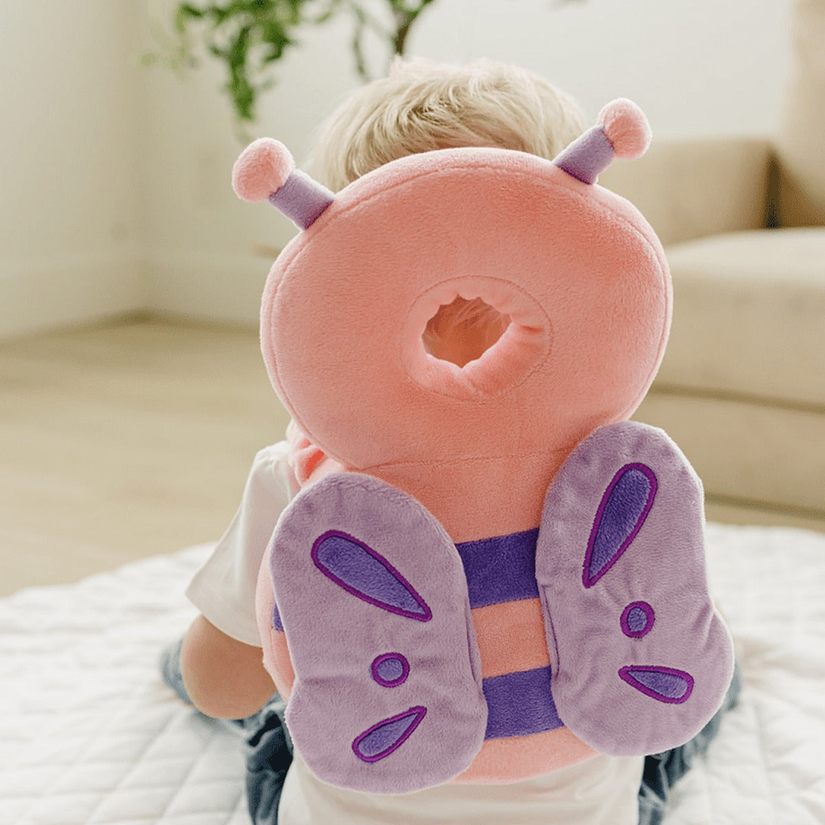 Toddler sitting on a play mat wearing the butterfly head protector backpack