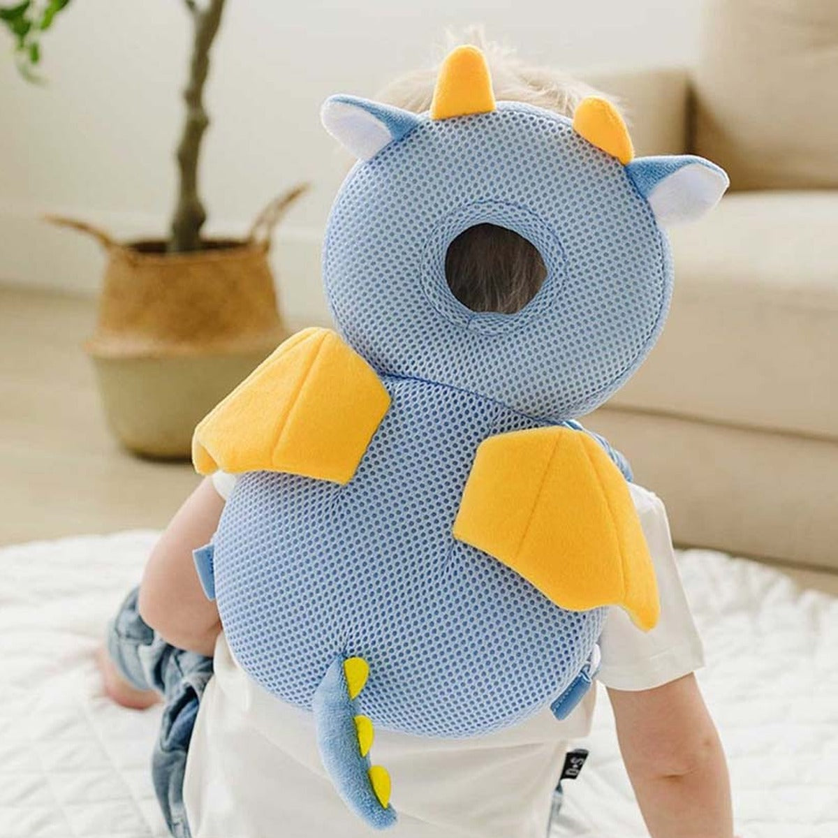 Toddler sitting on a play mat wearing the blue dragon head protector backpack